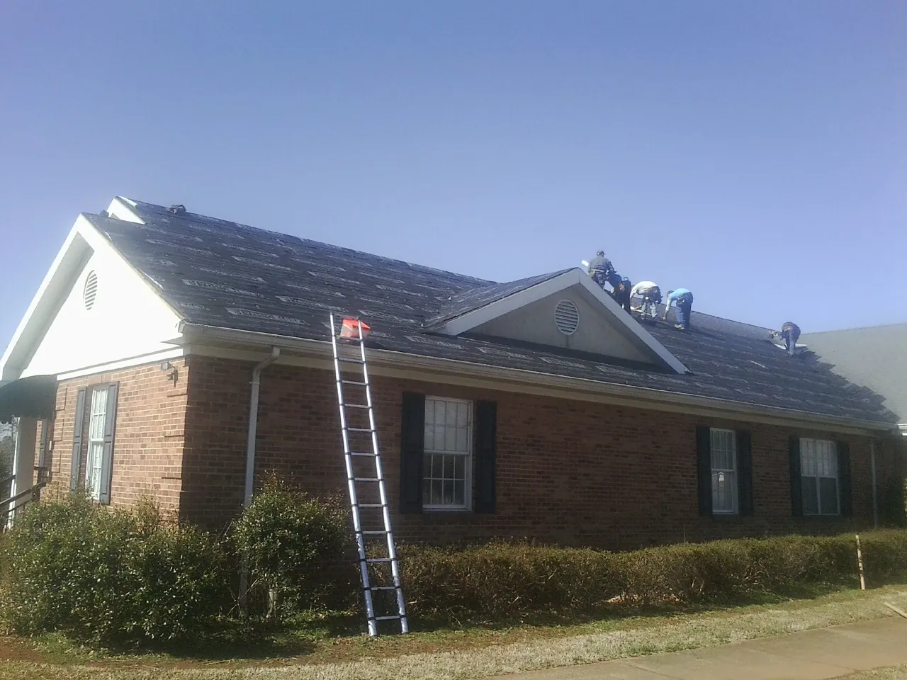 Crew tearing shingles off a brick ranch roof with a ladder set — Emergency Roof Repair work by our crew in East Bridgewater
