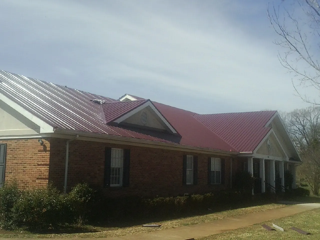 Red metal roof with gabled entries on a long brick building, from a Hail Damage Roof Repair job in East Bridgewater