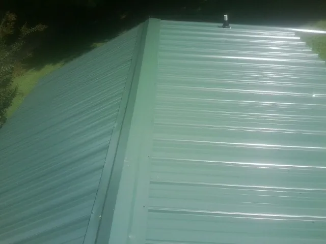 New green metal panels meeting at the ridge of a roof — Flat Roof Repair work by our crew in East Bridgewater