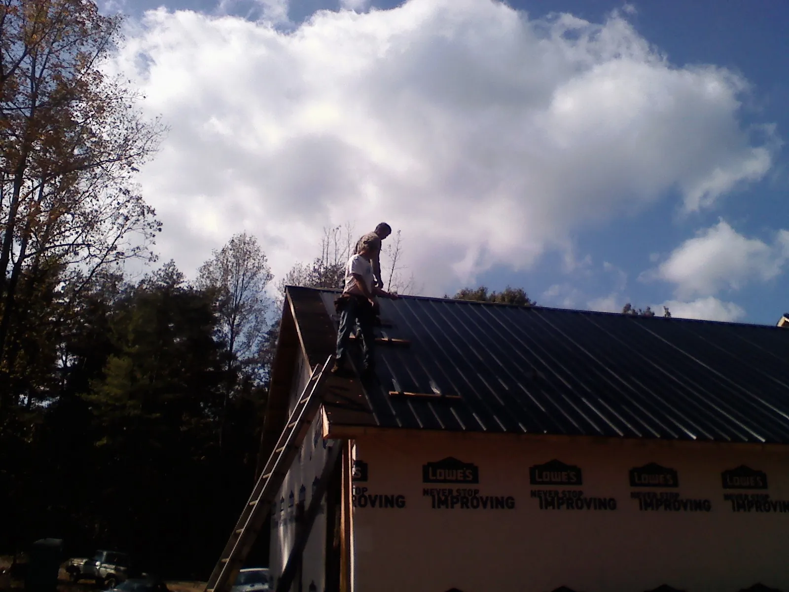 Roofer fastening dark metal panels high against a cloudy sky, from a Roof Inspection job in East Bridgewater
