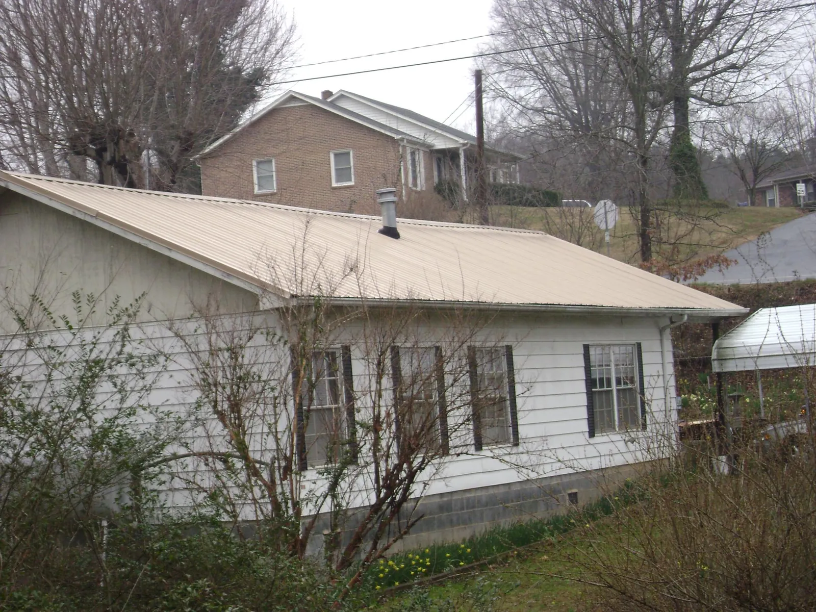 Tan metal roof on a white sided house set into a hillside — Commercial Roofing by Roofing Brothers in East Bridgewater